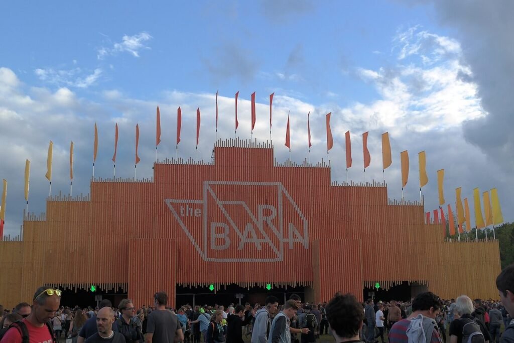 Festivalgangers voor het podium The Barn, een oranje gevel met vlaggetjes, op Rock Werchter